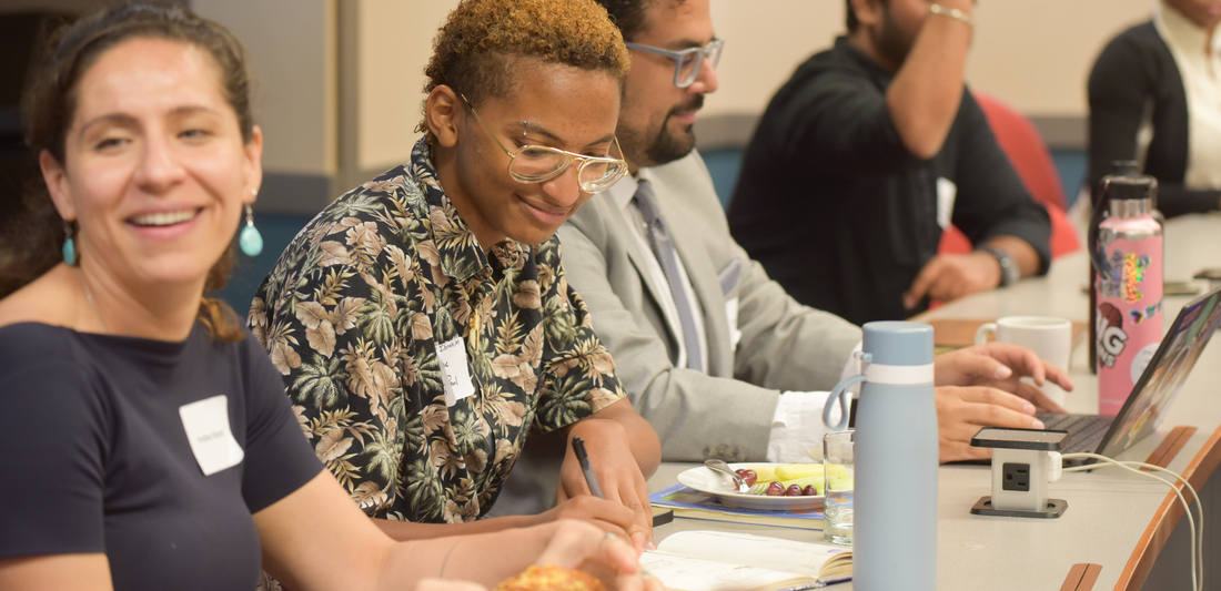 at a table, three professionals are engaged in a panel presentation. they are young and racially diverse, and seem engaged in teh conversation