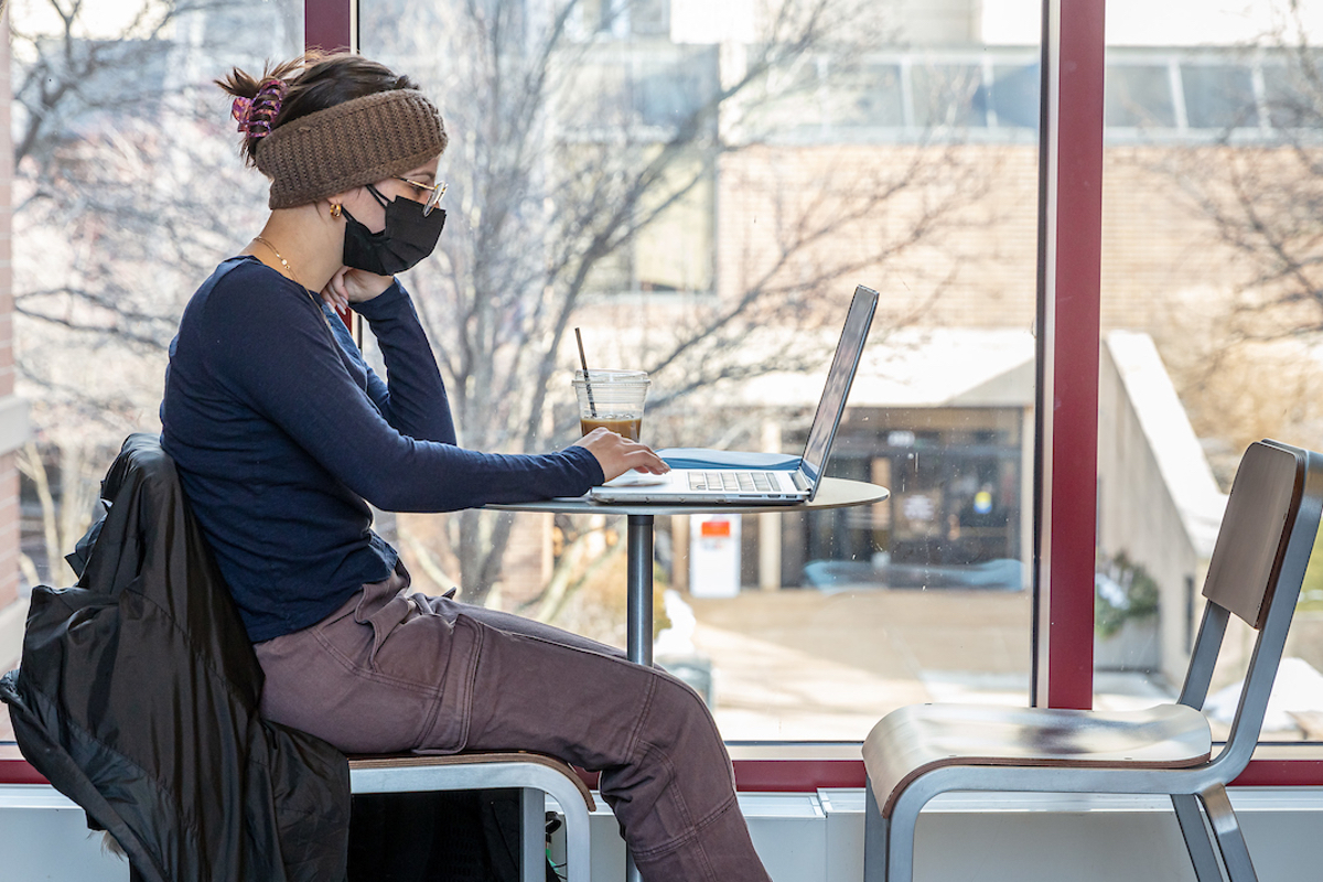 A student sits with a laptop by a window