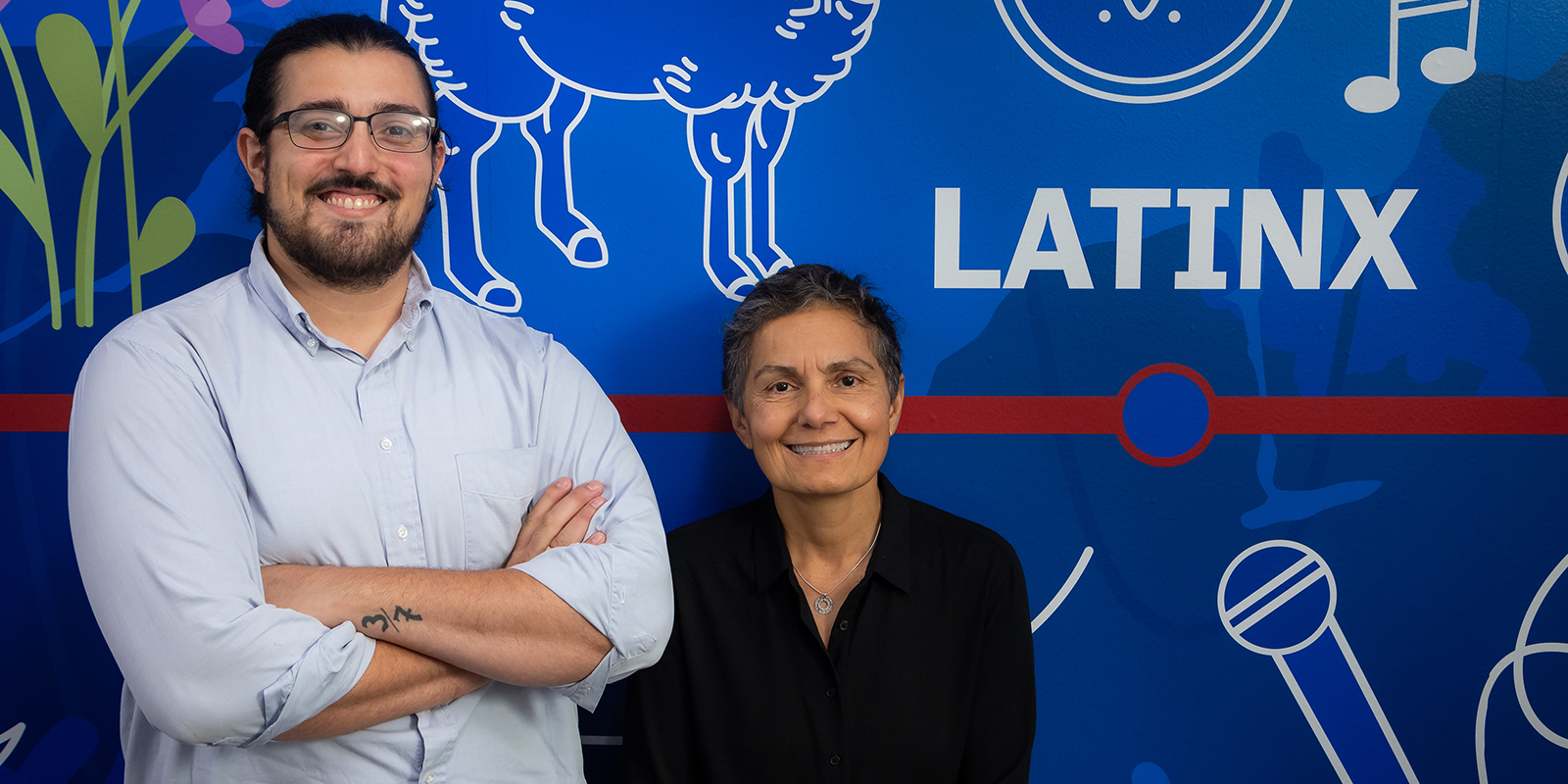 Lourdes Torres and Vincent Peña stand in front of a mural in the Latinx Cultural Resoruce Center at DePaul.