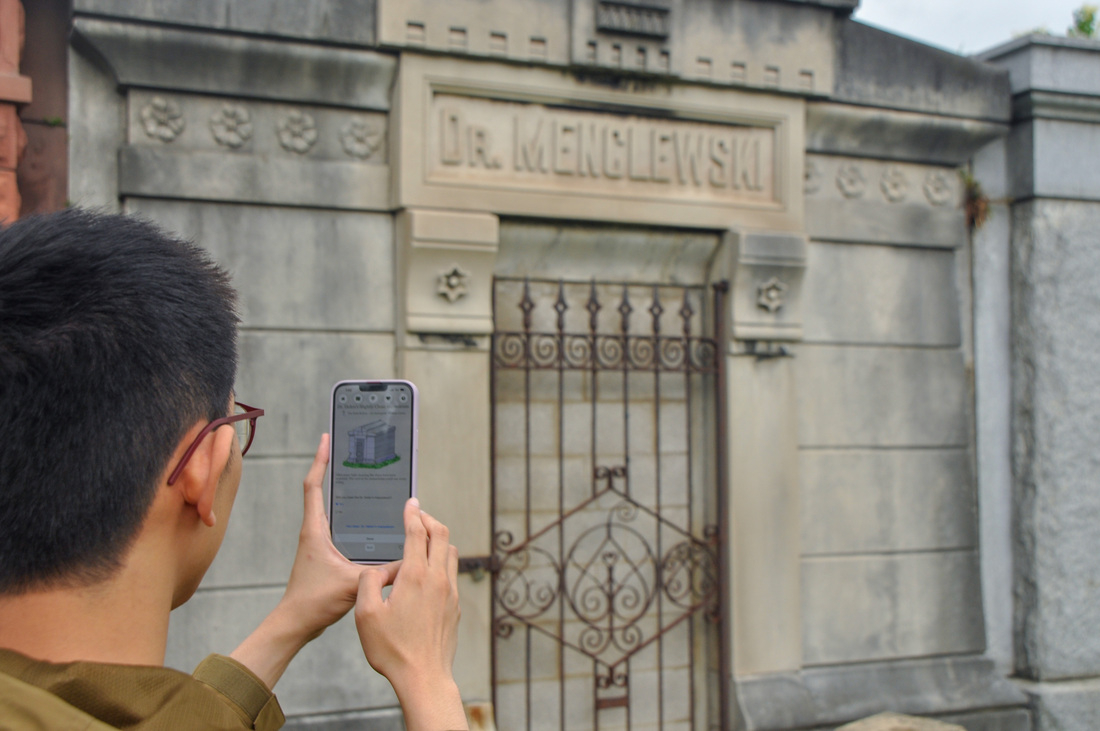 Student holds phone in front of historic site at Graceland Cemetery