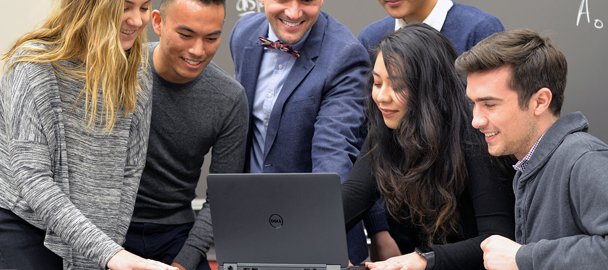 Professor Jim Mourey looking at a computer with students in a classroom