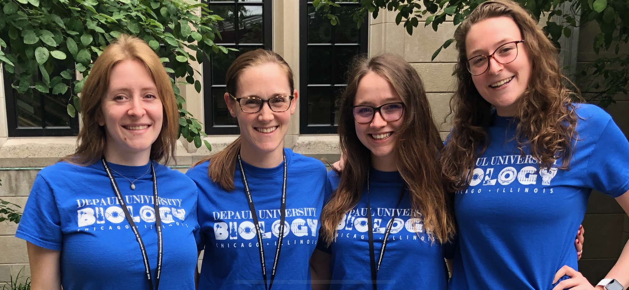 Margaret Bell and three students, all wearing blue shirts, standing and smiling for a picture.