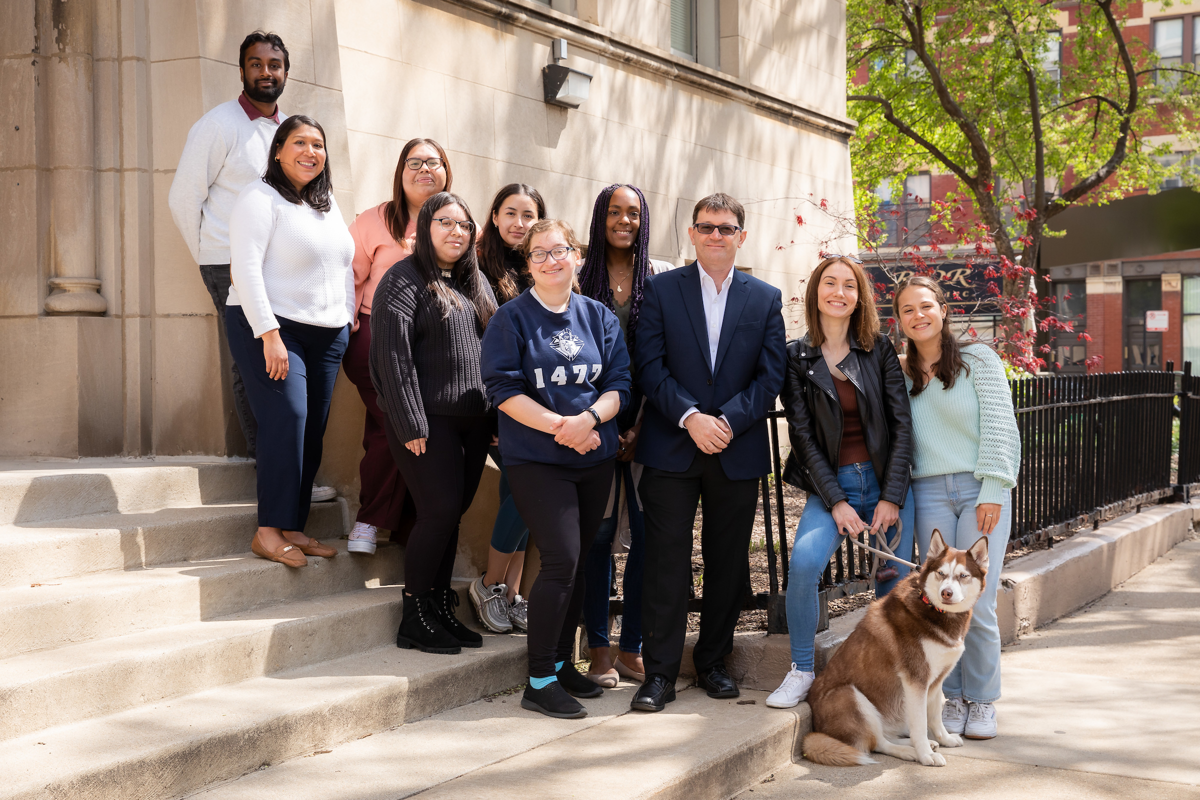 Students and Antonio Polo standing on the front steps of Byrne Hall on a spring day with a dog