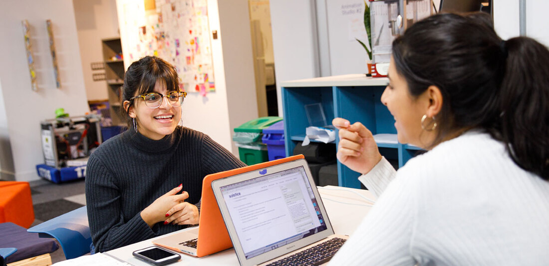 two students with laptops open smiling and ta