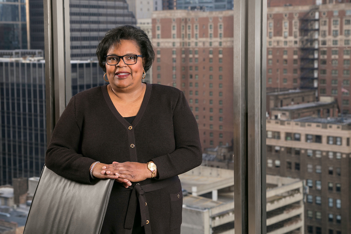 Linda Blakley stands behind a chair in front of a window showing Chicago