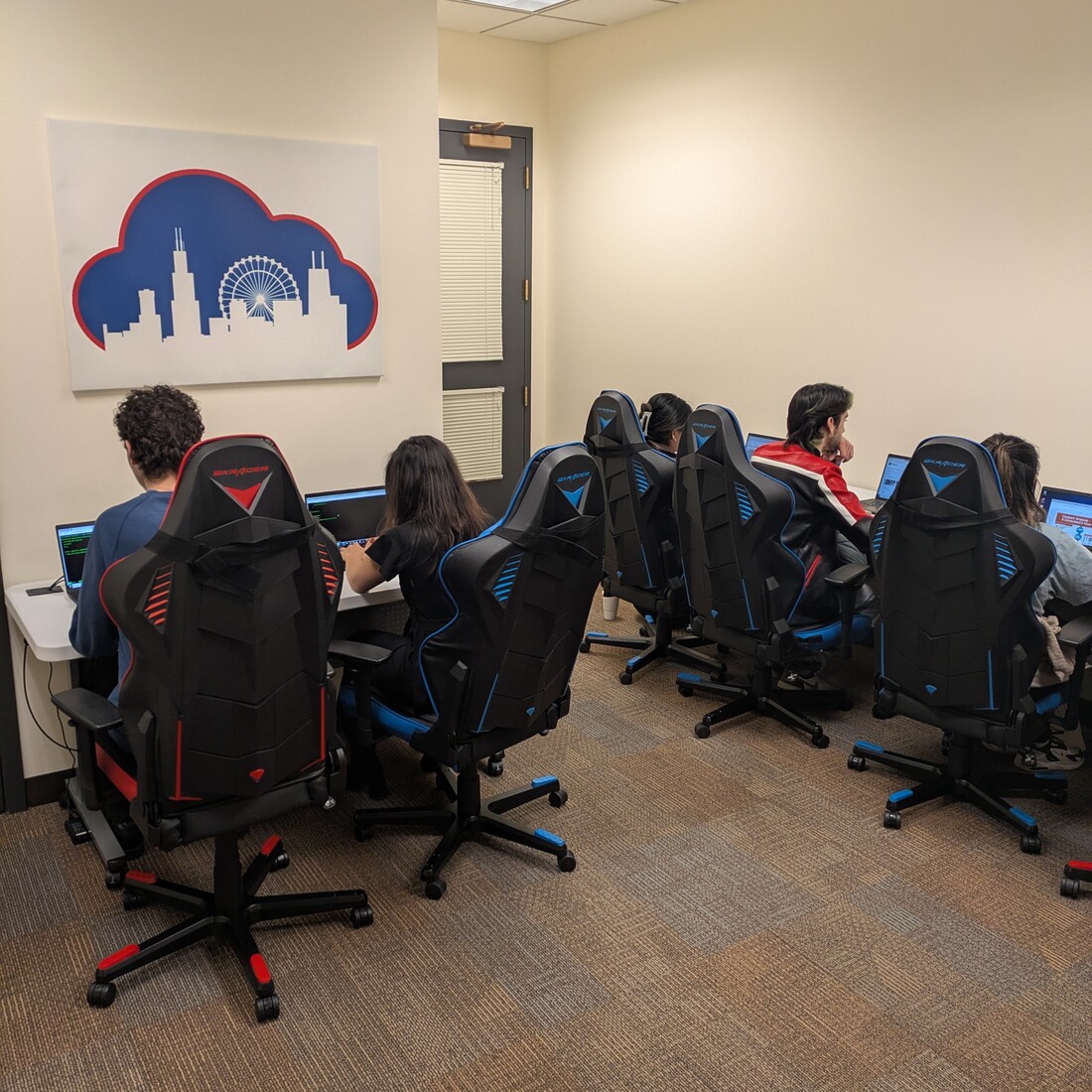 students sit at tables in state of the art, bright blue and red ergonomic computer chairs