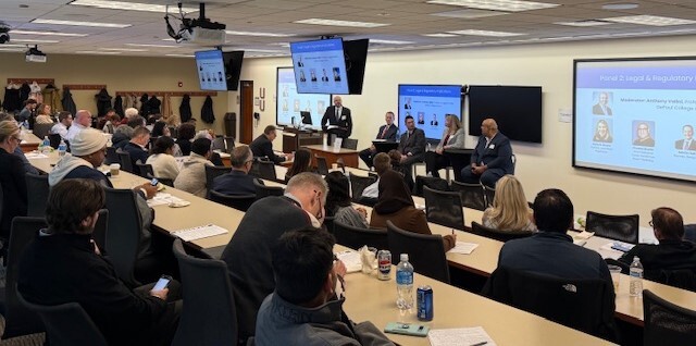 a lecture hall with attendees in business casual watching a panel of four people