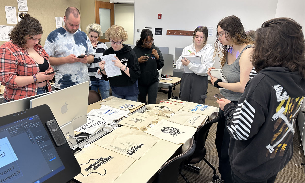 Graphic design professor Sajad Amini standing around a table with designs printed on tote bags