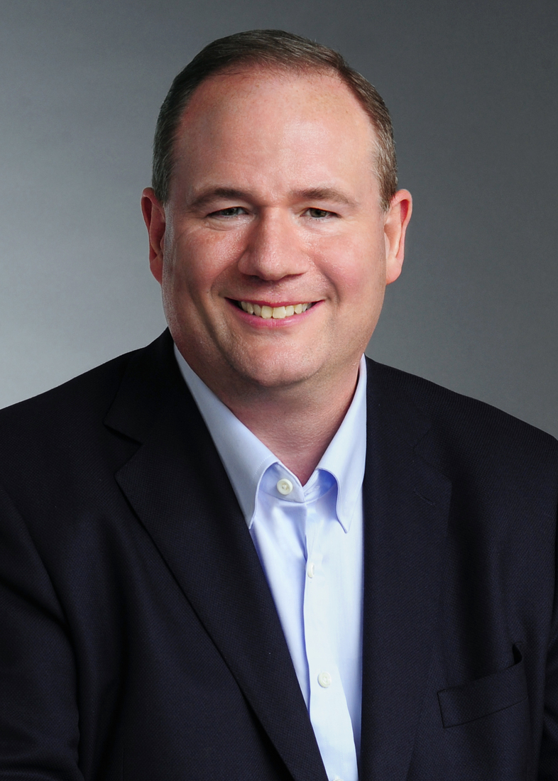 Cory Gunderson, a white man in his fifties smiling in a crisp navy suit