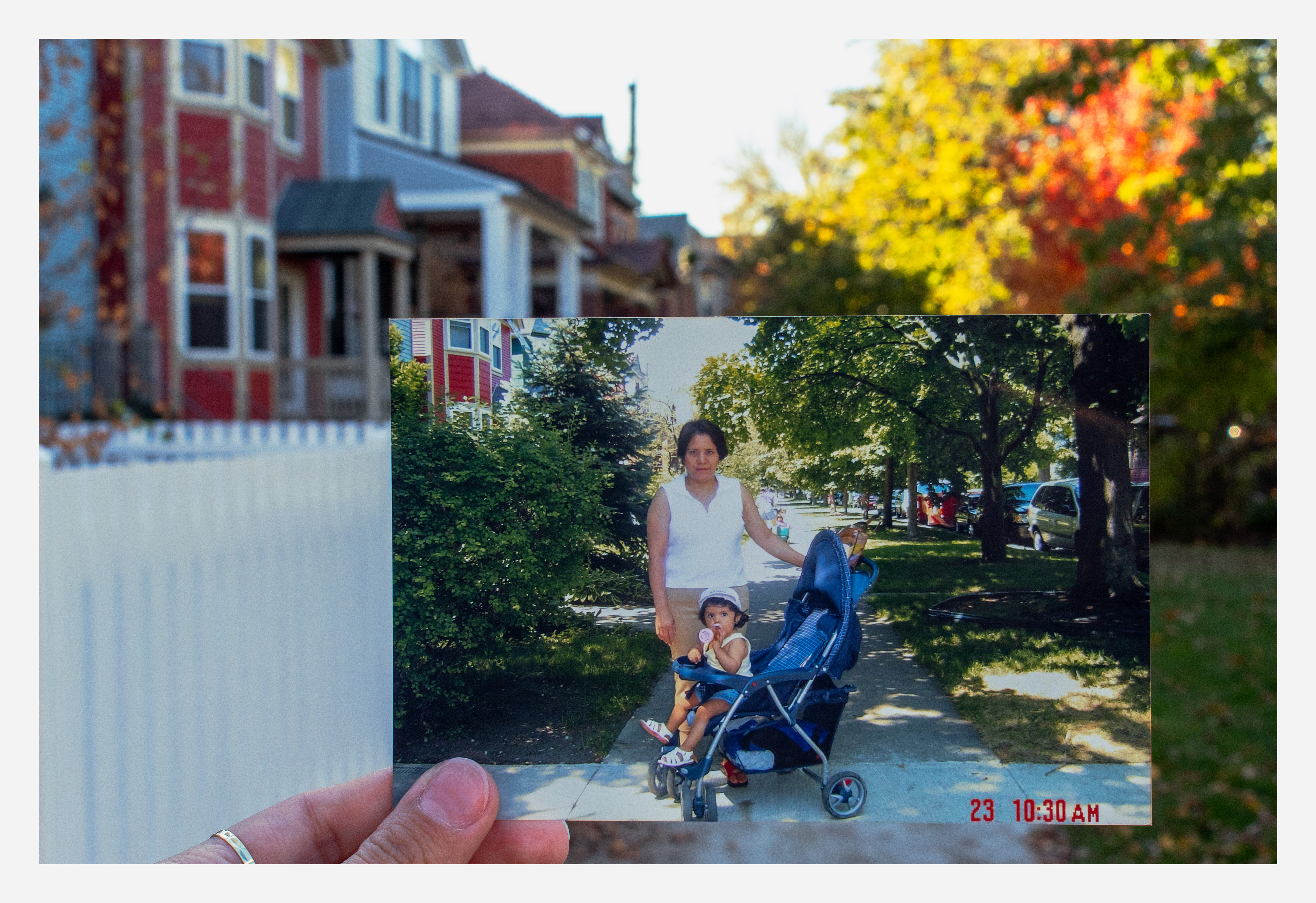 Daniella's hand holds up a childhood photo of her mother standing in the sidewalk with toddler Daniella in a stroller. The sidewalk lines up with the same sidewalk in the present day.