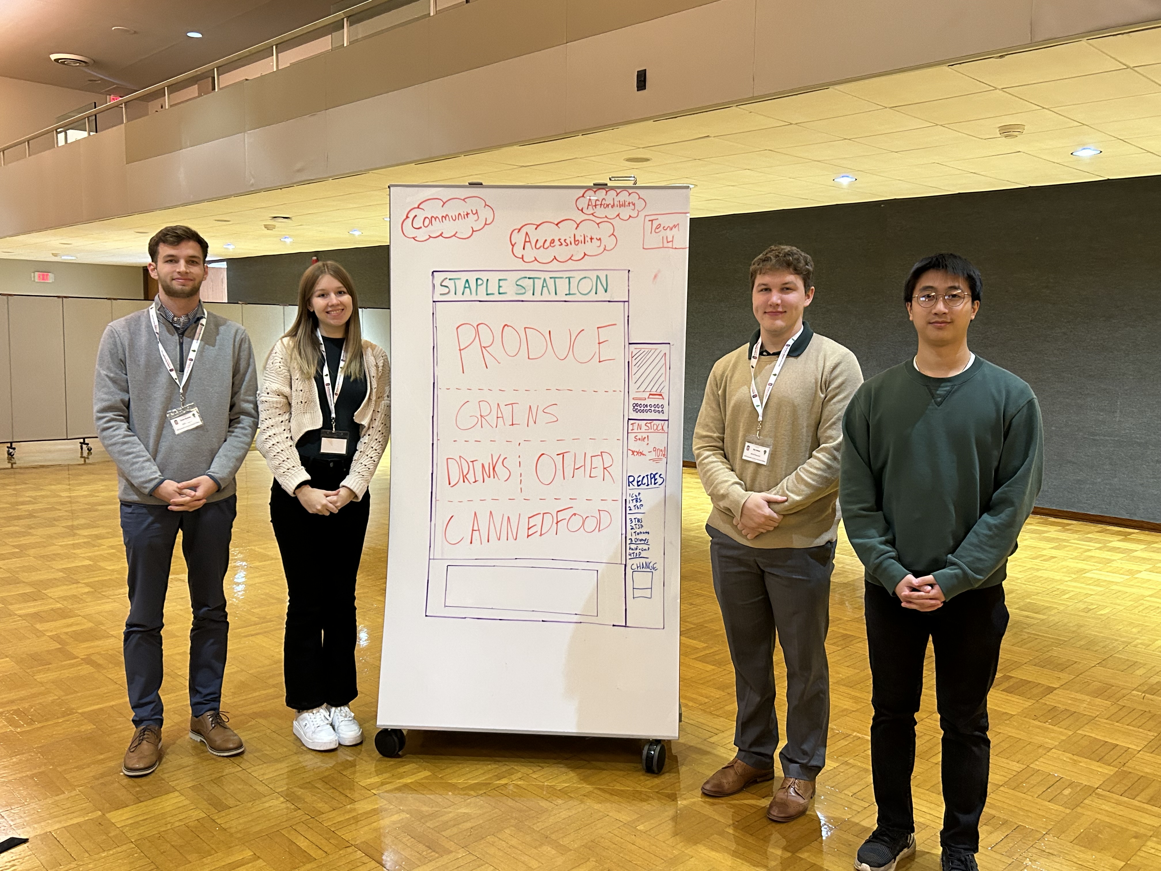 Four students pose in front of a poster with a drawing of a food vending machine