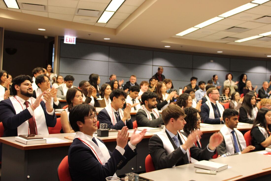 a group of students in suits and white stoles clapping in a lecture hall