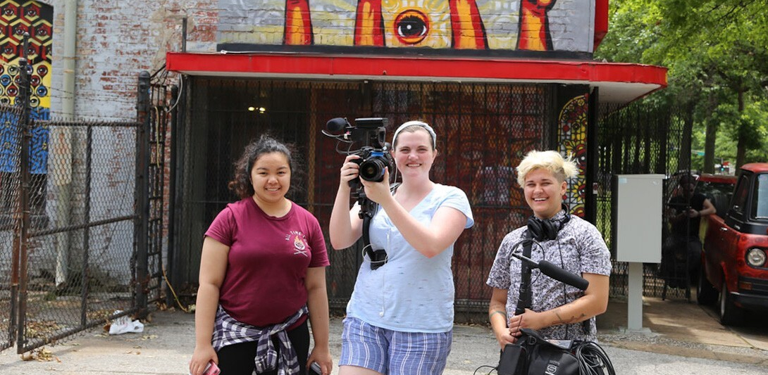 Three students with film equipment pose for a photo outdoors