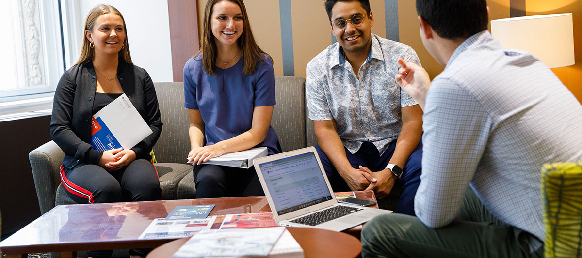 A group of students sitting down around a table and talking to each other.