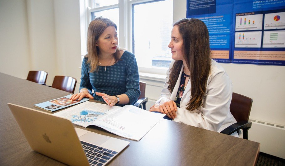 Two women seated at a desk, facing each other mid-conversation
