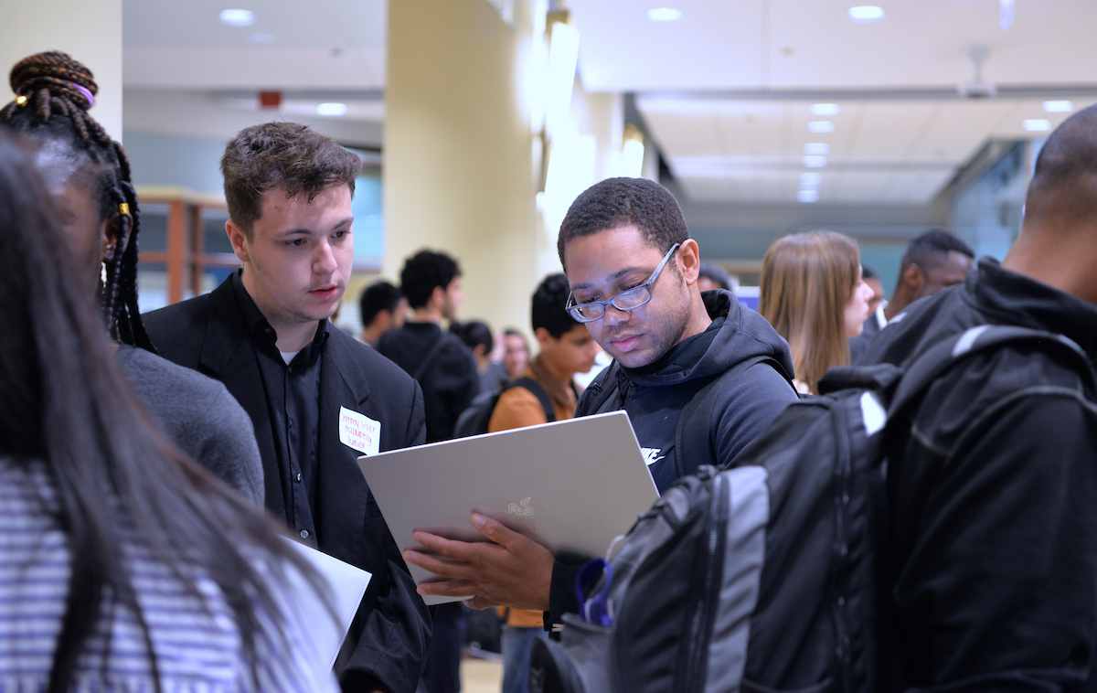 In a bustling atrium, a student looks down at an iPad