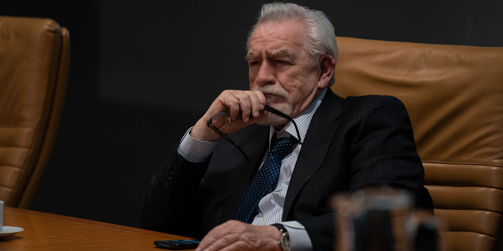 Brian Cox sits at a conference table scowling