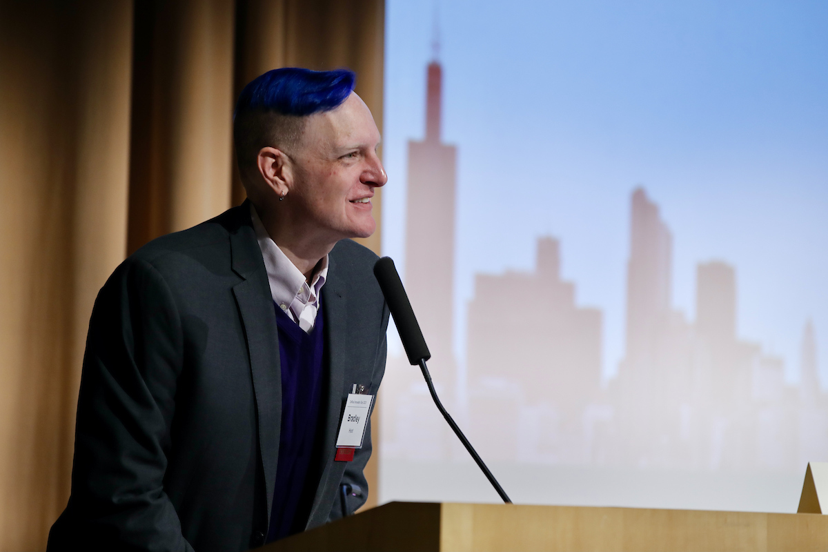 Bradley Hoot stands at a lectern with an illuminated screen behind him.