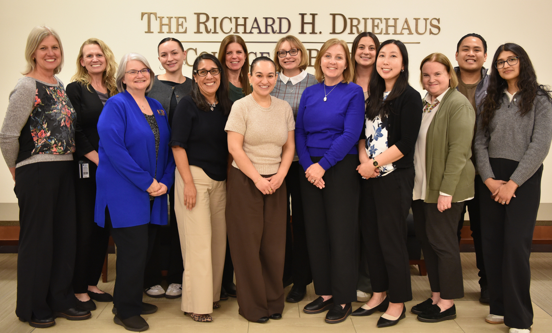 the driehauss academic advising team pose in business casual in front of a sign, partially visible, reading the richard h. driehaus college of business