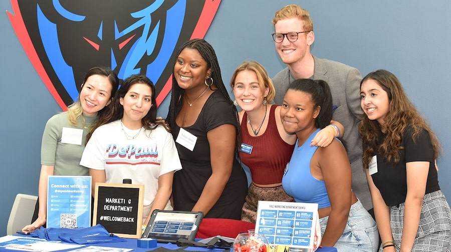 A group of students posing together behind a table during the Driehaus Open House event