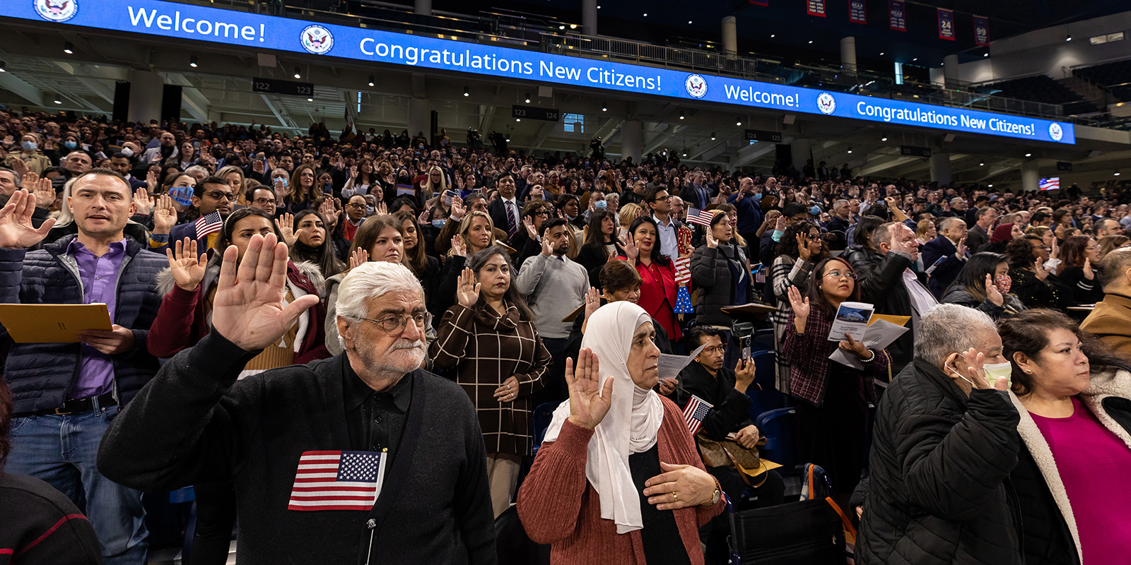 Dozens of new citizens hold their right hands up as they participate in a naturalization ceremony at Wintrust Arena.