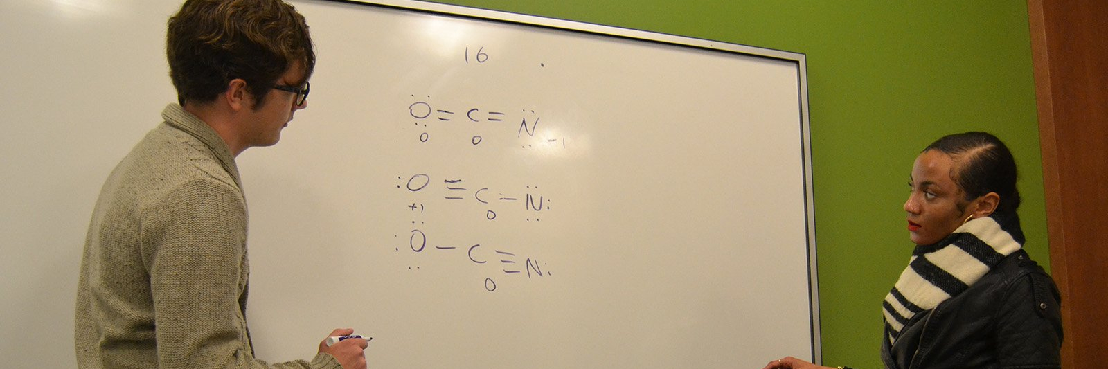 Two students discussing class materials on a white board.