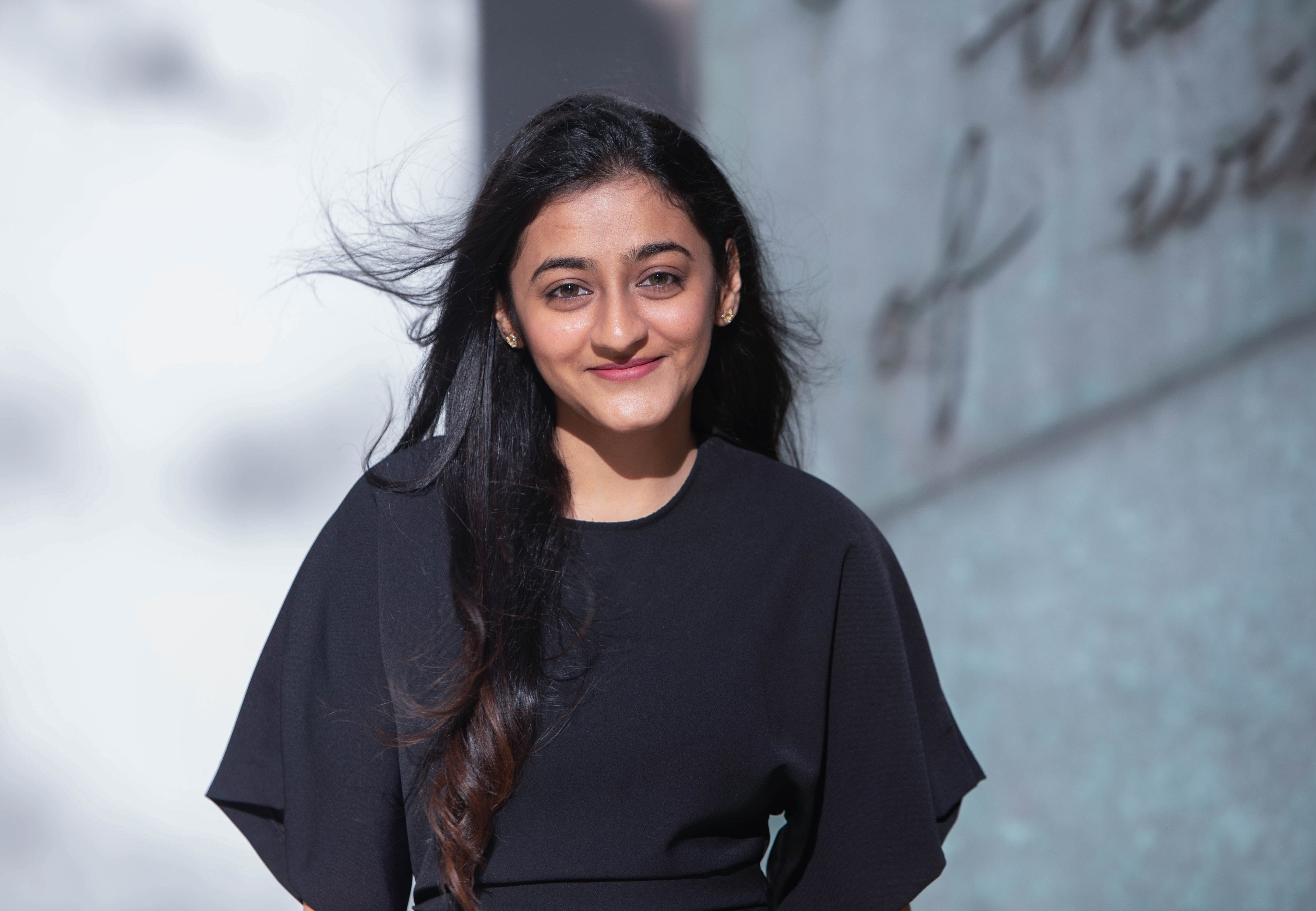 Commencement speaker Kreena Shah standing outside wearing a black top with flowy sleeves and a bit of wind in her hair.