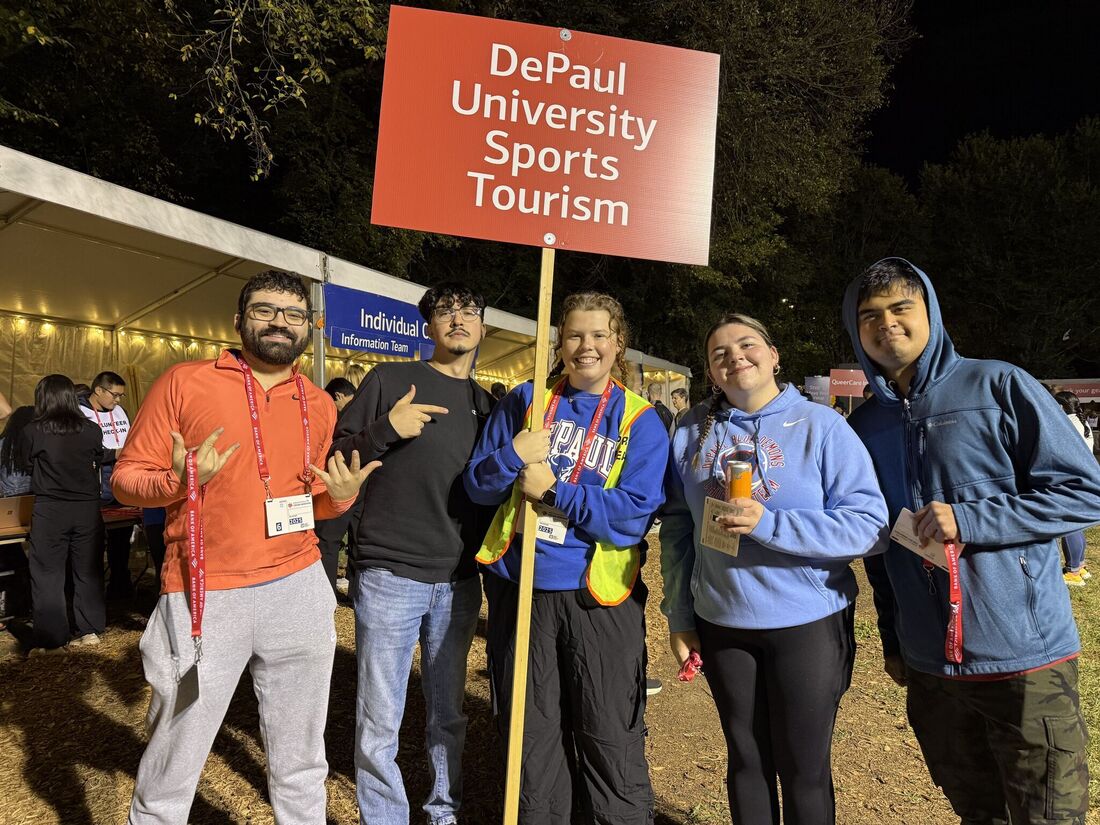 a group of students in jackets pose in a park pre-sunrise with a sign reading DePaul University Sports Tourism