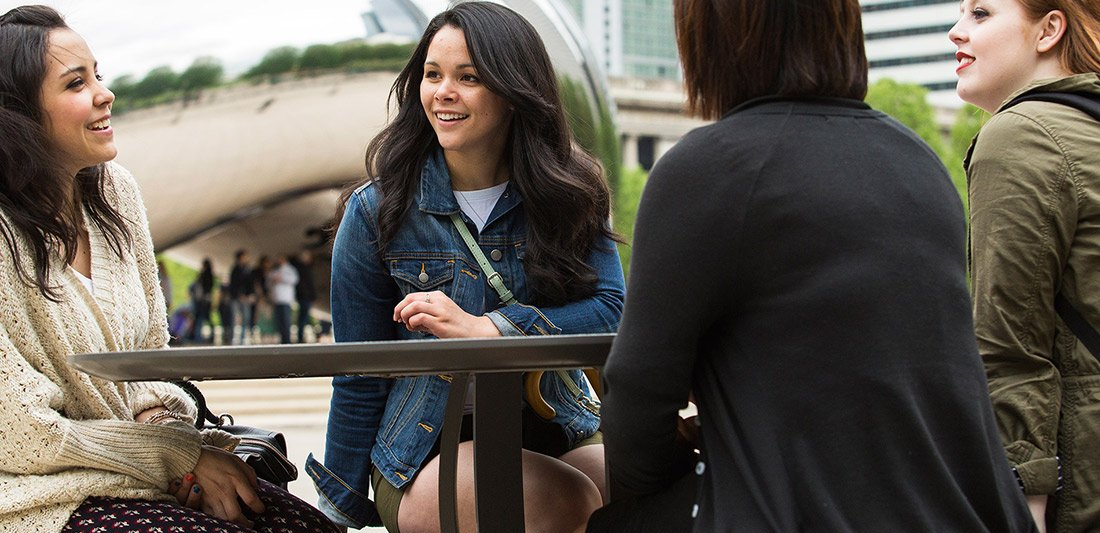 Four students seated outside with the Chicago Cloud Gate sculpture in background