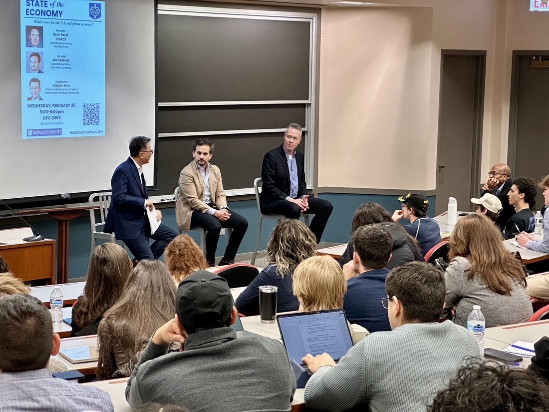 a room full of people listen to a panel hosted by three men in suits