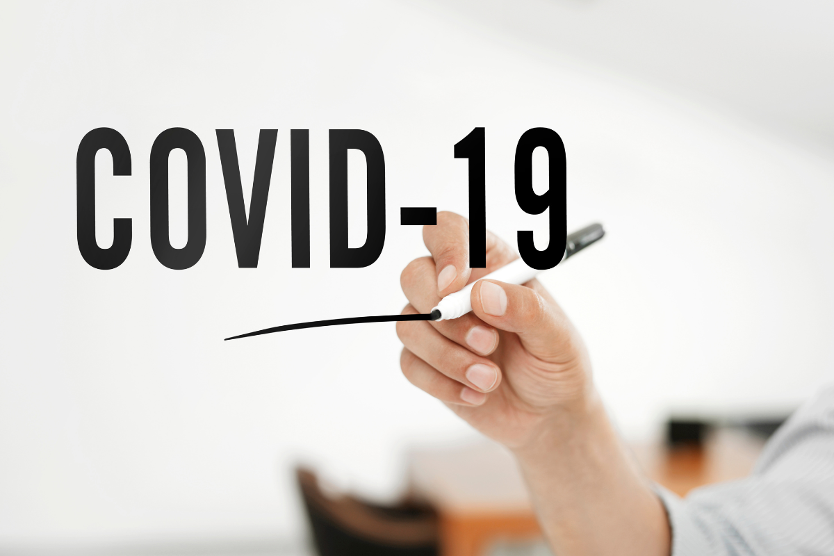 A person writes the words Covid-19 on a glass wall