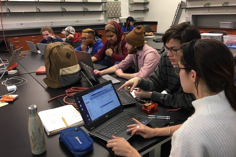 A group of students discussing class materials in front of their computers.