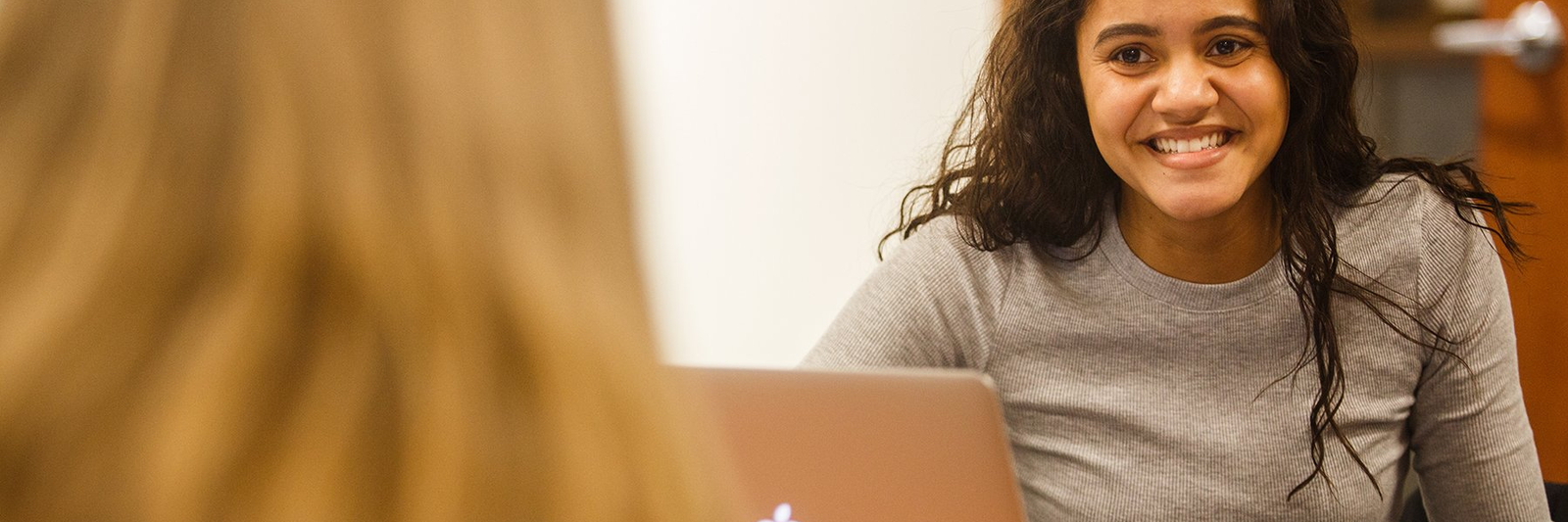 A student smiling while listening to another student.