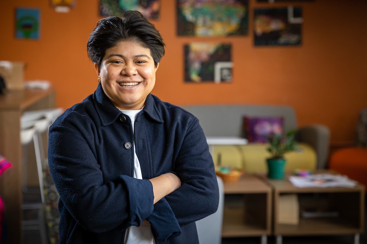 Emily Hurtarte stands with arms crossed, wearing a blue jacket over a white T-shirt.