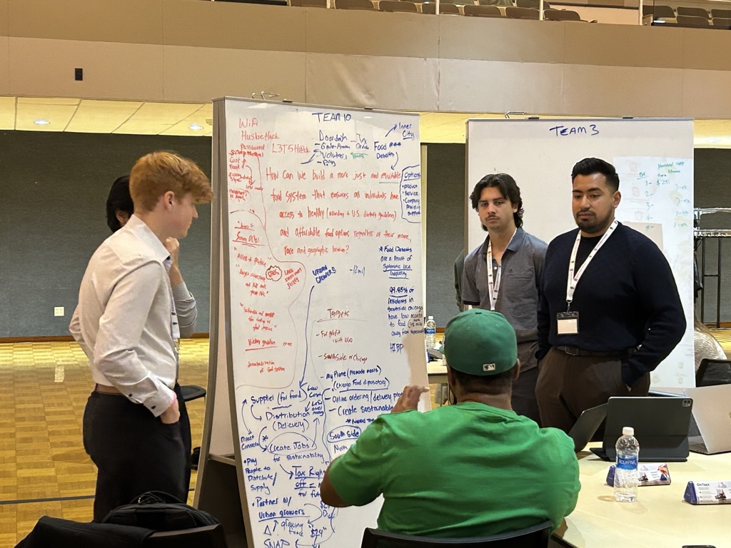 A group of the students who attended the NIU hackathon pose in front of a stage in a small auditorium