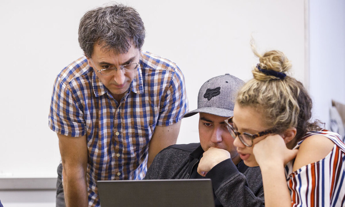 Two students review their project with a professor on a laptop