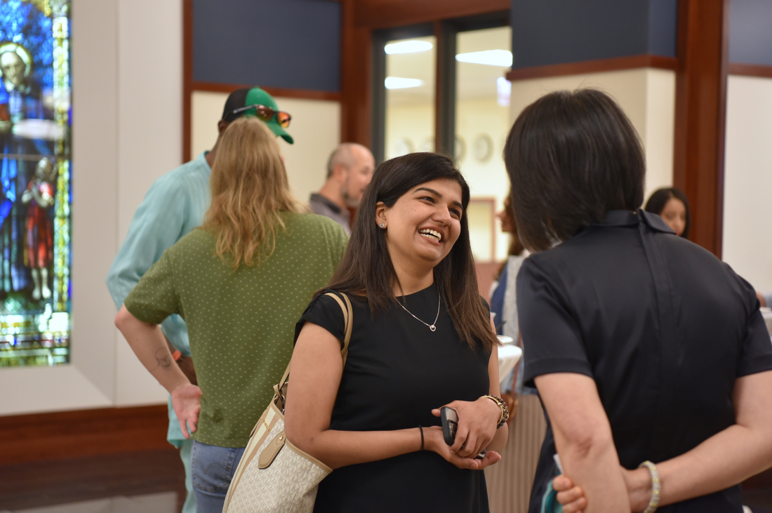 A college student mid-convesation smiling, with other people and some beautiful stained glass in the background