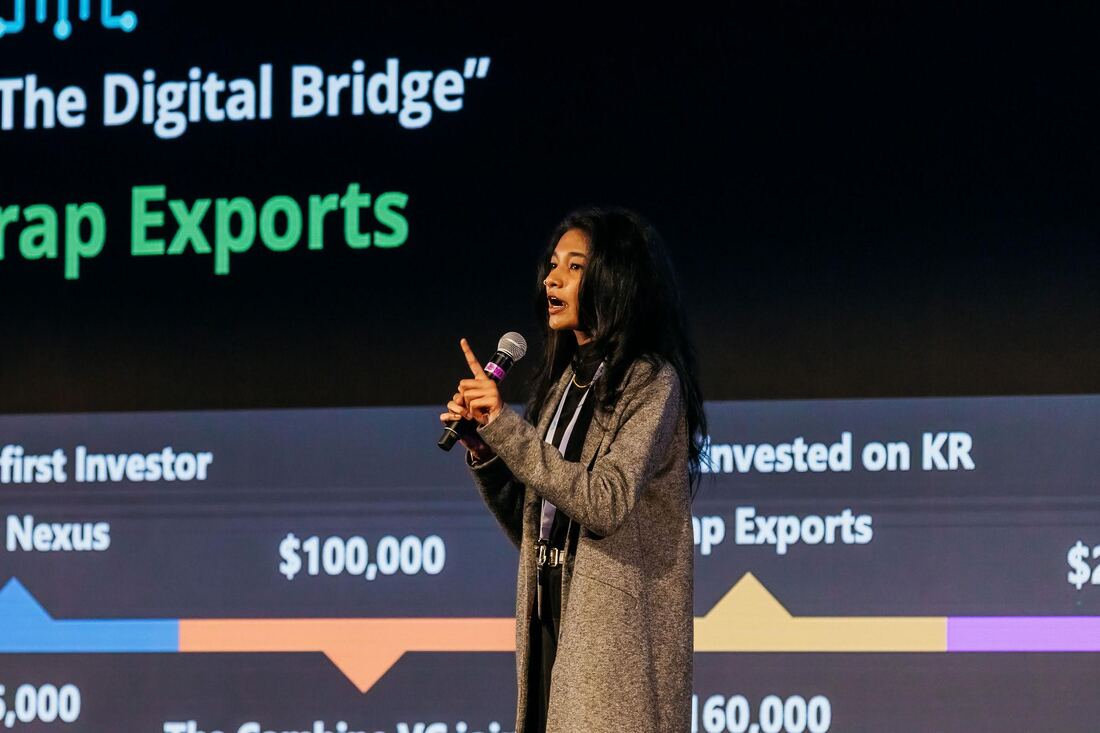 A young woman in a blazer presents on a stage; a timeline of a firm with associated milestones is behind her