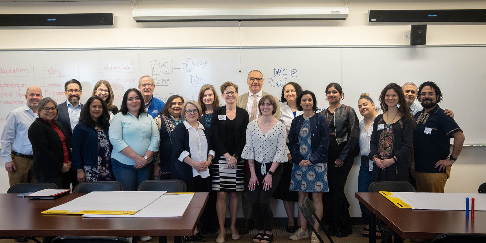 A dozen DePaul professors, staff and administrators post in front of a whiteboard after a meeting