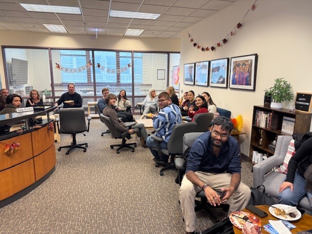 a brightly lit office reception area full of students and faculty enjoying paper plates of food
