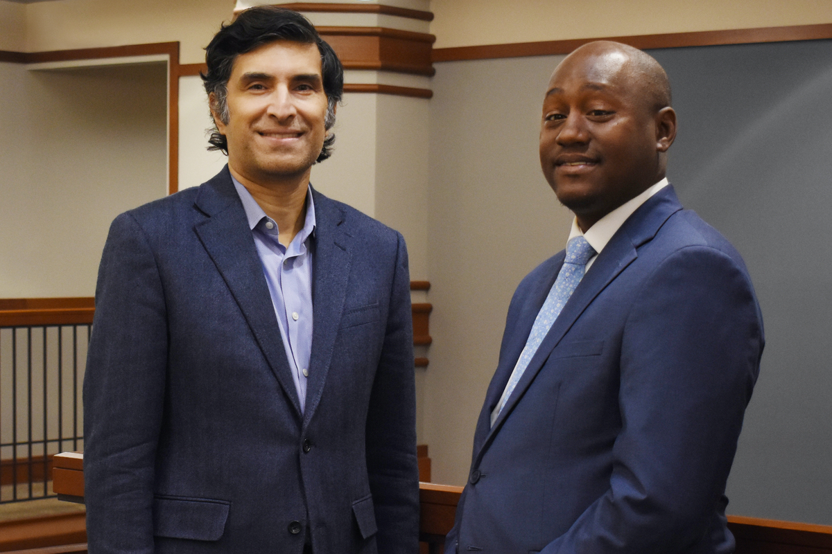 Two men in suits stand in the law school atrium.