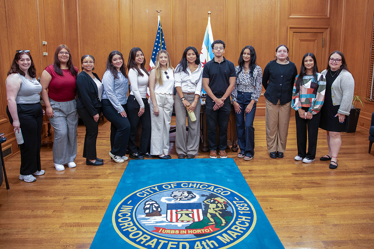 A group of students stand in a city hall office in front of branded city hall rug