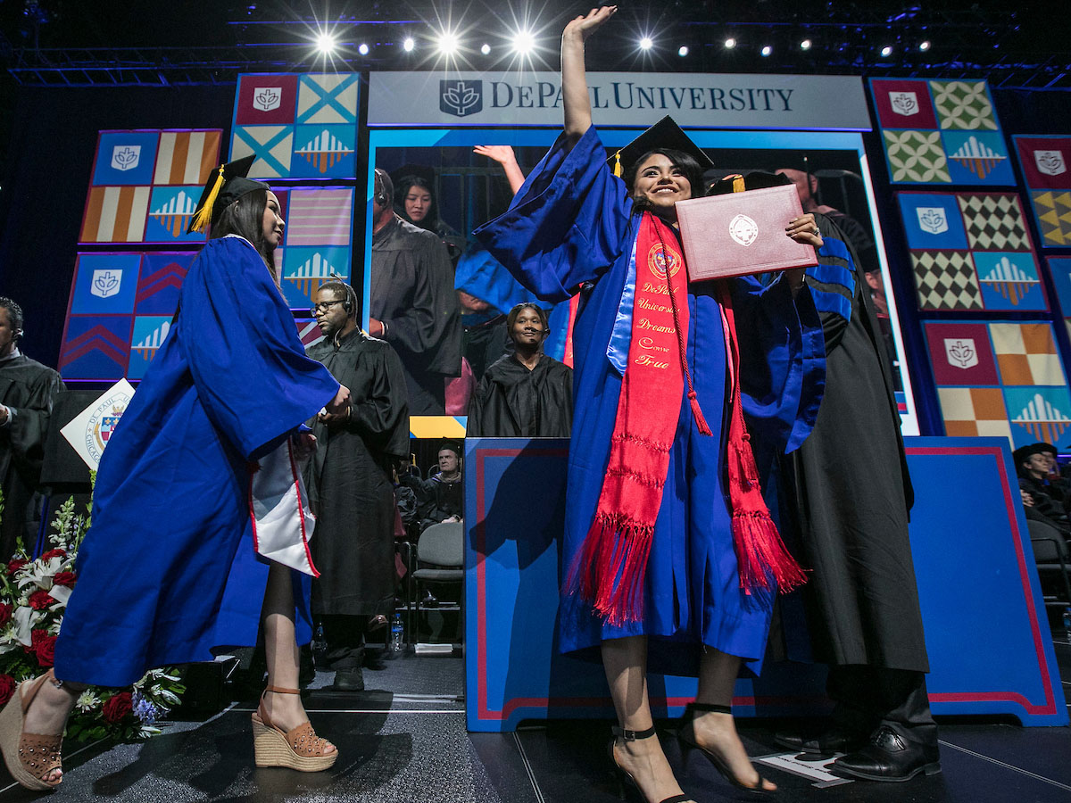 Graduate walks across stage with diploma cover waving to the audience