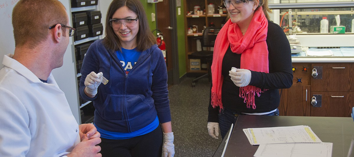 Three students holding samples in a lab while laughing.