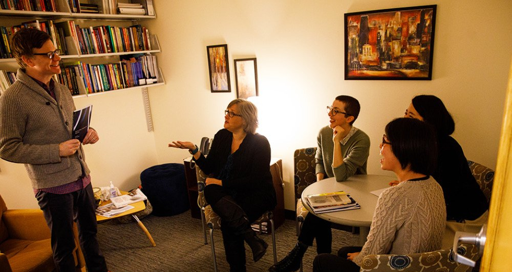 DePaul SCPS adults students sitting around a table with a professor listening to their peer speak.