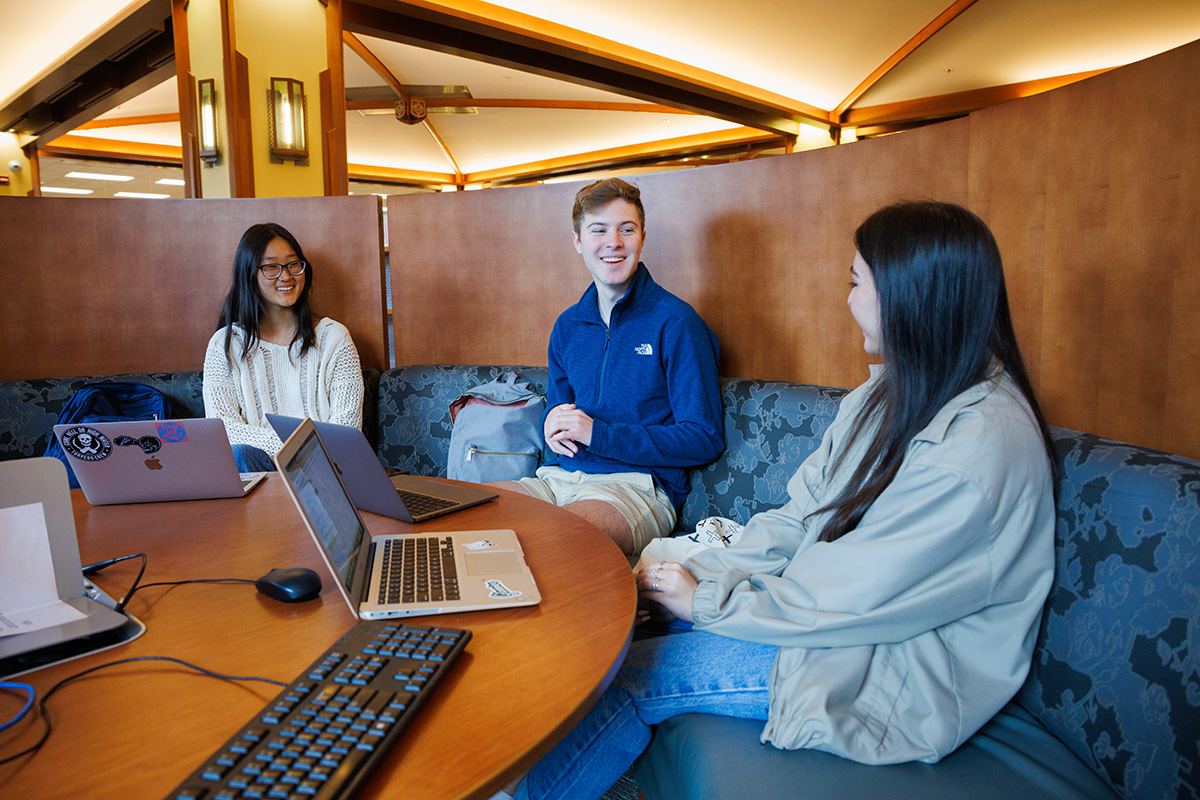 Three students sit talking in a booth in the library