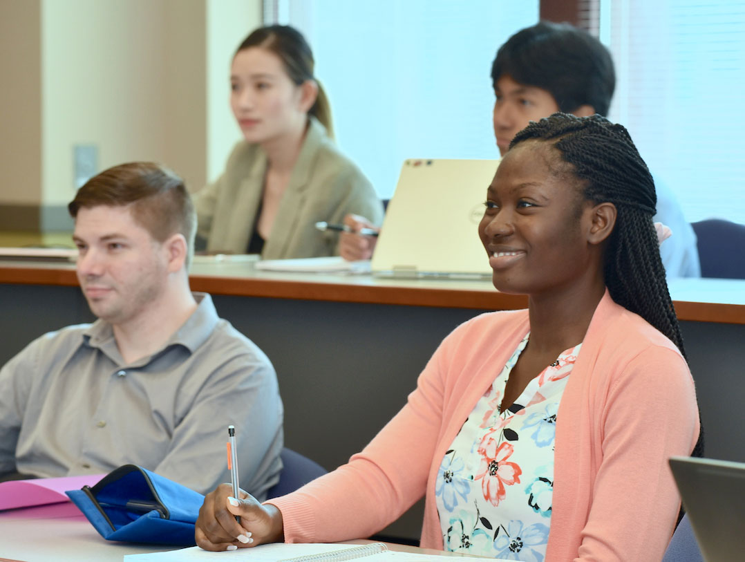A student sitting at a desk and holding a pen, smiling.