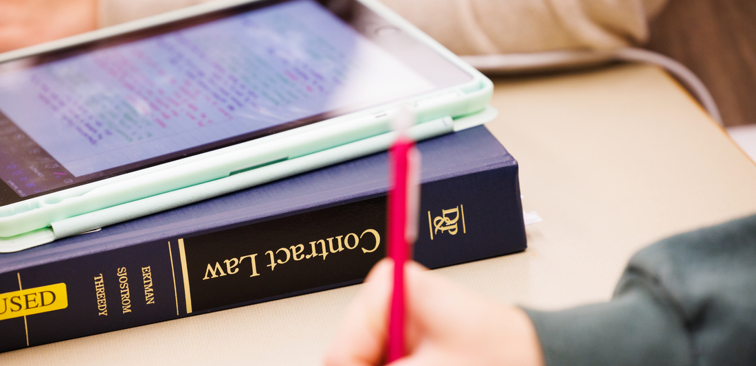 DePaul Law Student Writing with Contracts Book on Desk