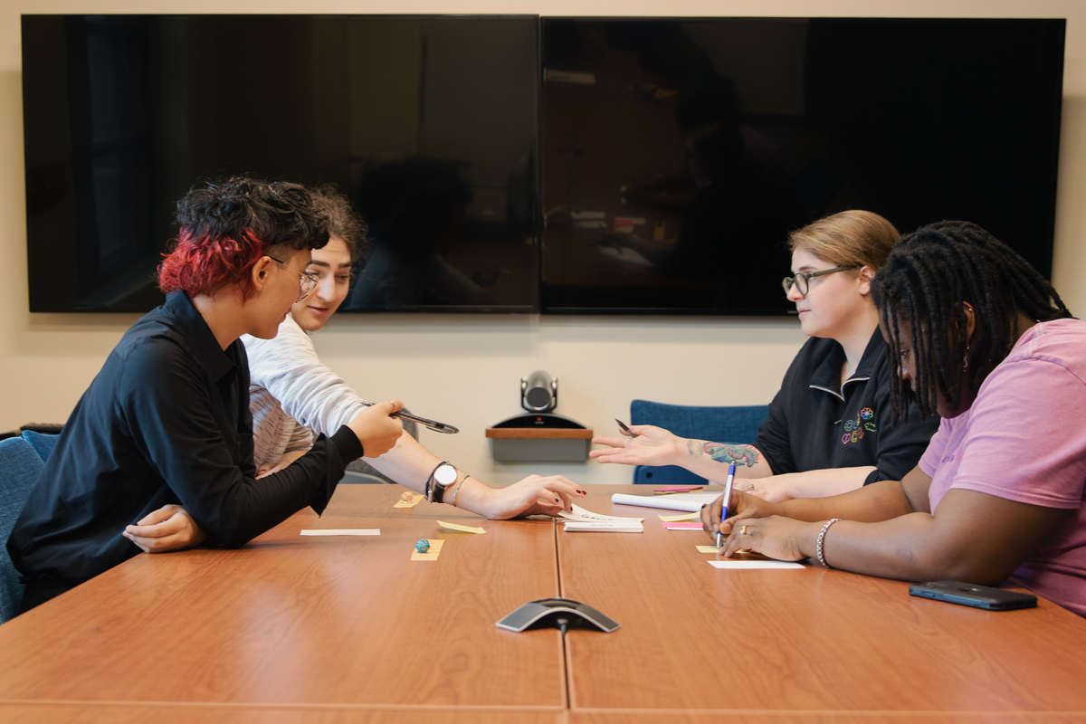 Students play a board game across a wooden table.