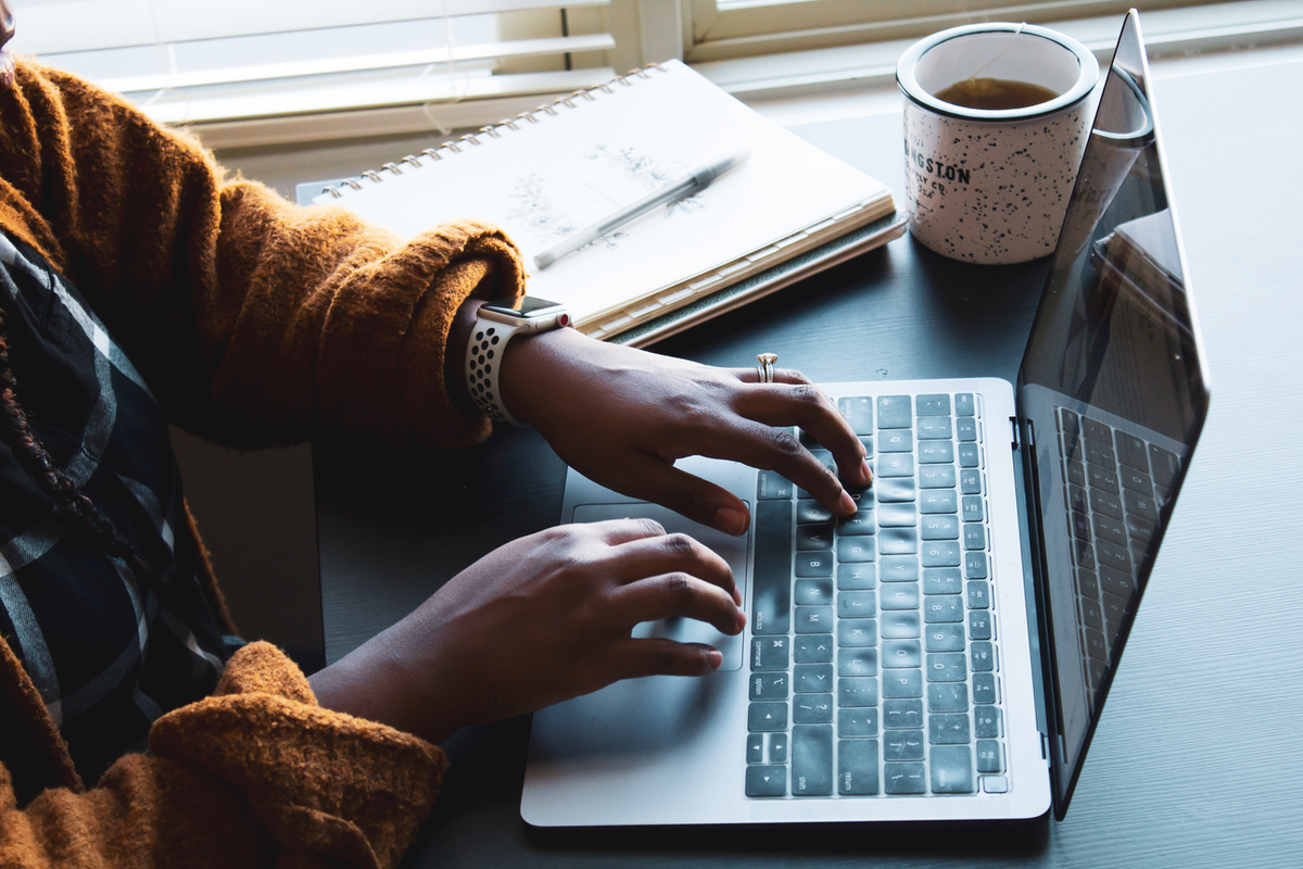 Woman types on a laptop with a notebook and mug nearby